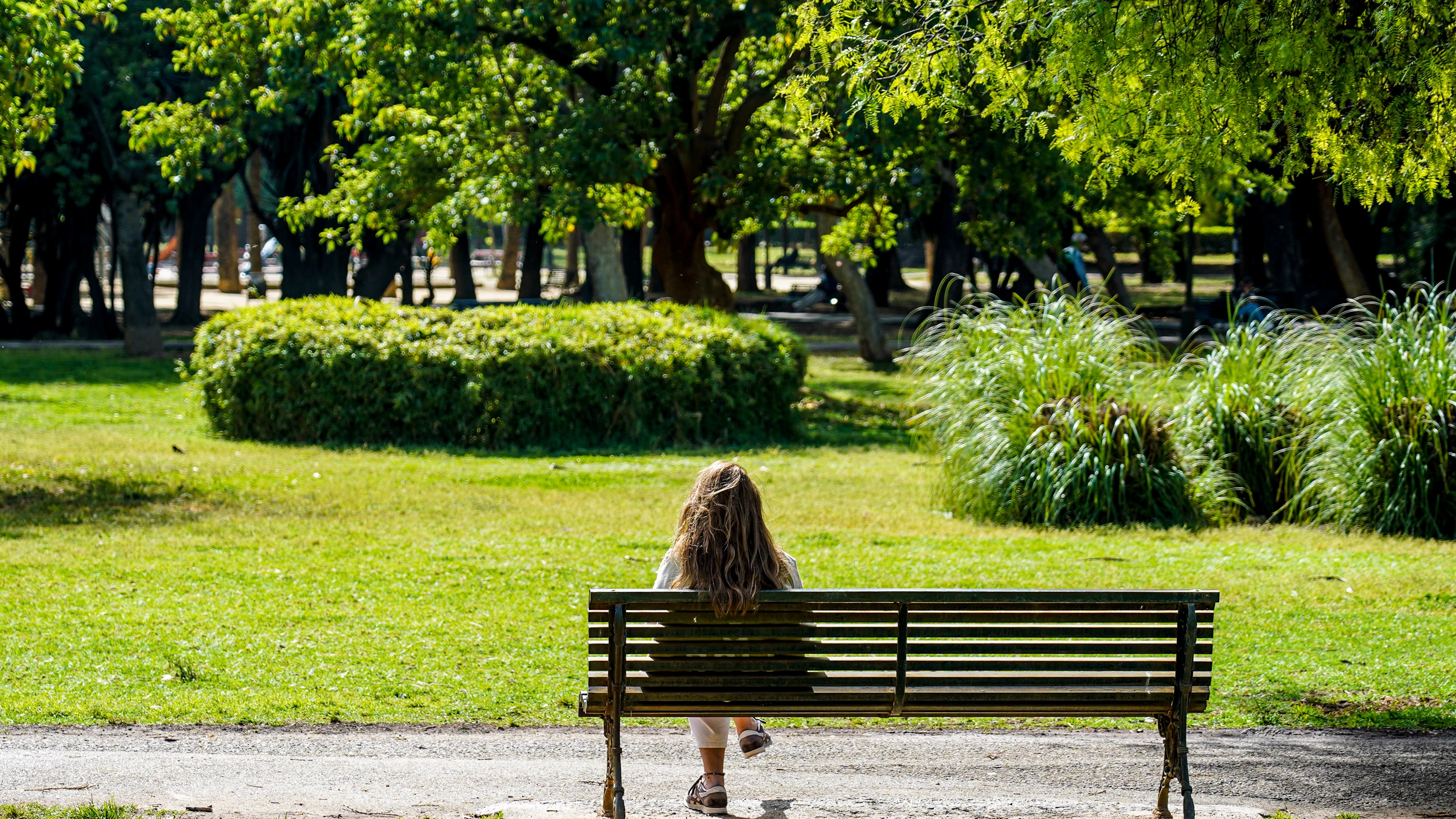 Una mujer toma el sol en un banco del Parque de Los Príncipes, en un día donde continúa el tiempo seco y soleado.