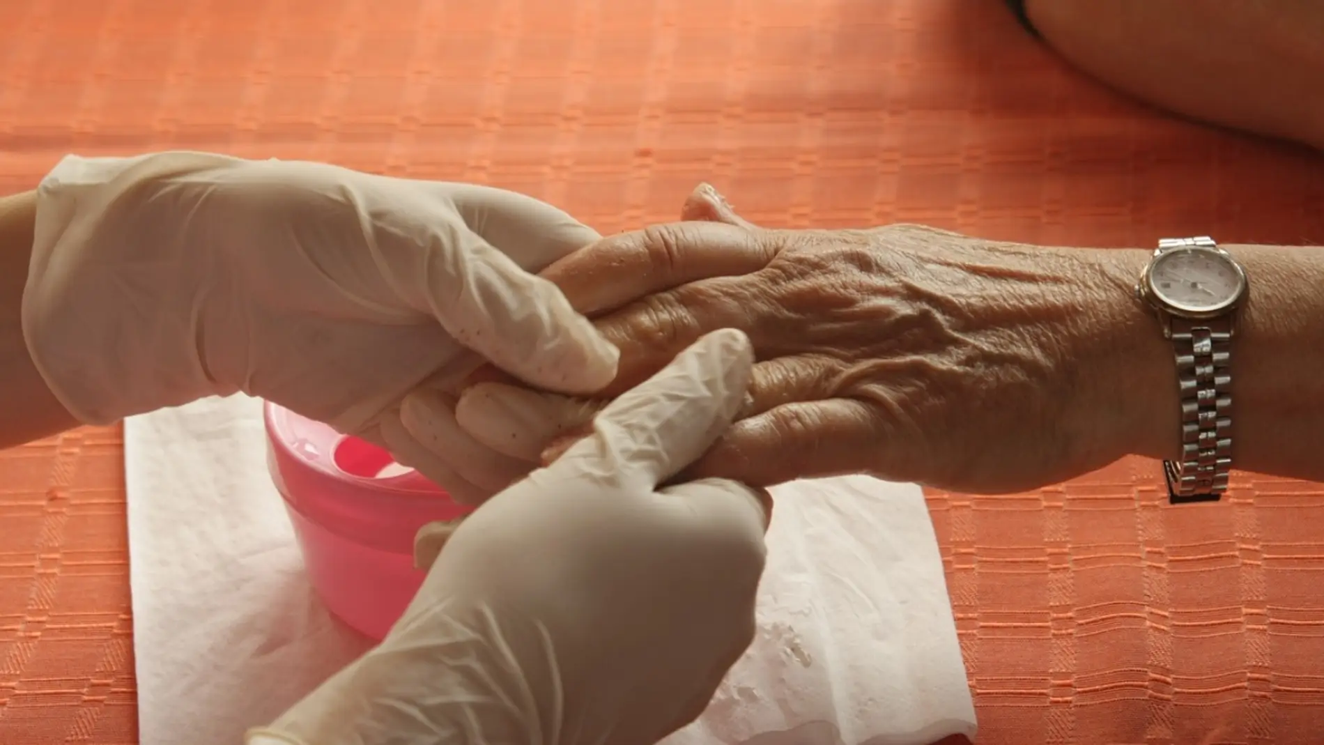 Una mano de una persona anciana sostenida por una cuidadora