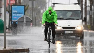 Un hombre en bicicleta se resguarda con un chubasquero bajo la lluvia en el municipio almeriense de Aguadulce.