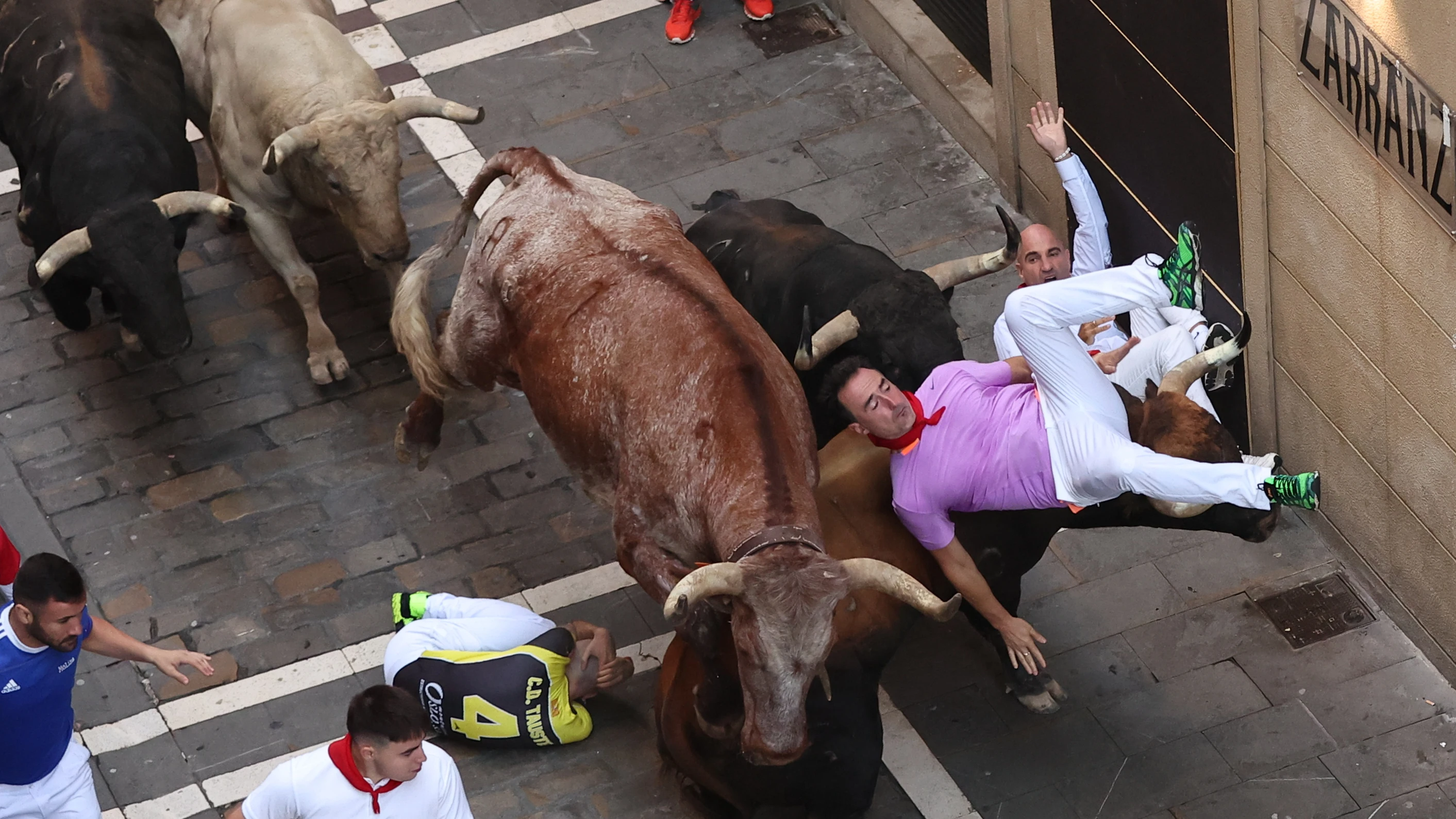 Un mozo volteado por un toro, en el tramo la curva de Mercaderes al inicio de Estafeta, durante el cuarto encierro de los Sanfermines 2023