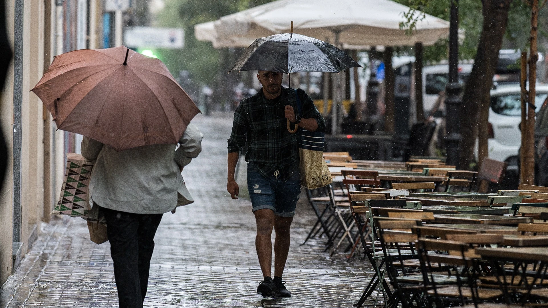 Varias personas se resguardan de la lluvia con paraguas en Madrid.