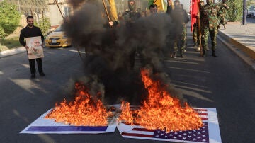 Las banderas nacionales de Estados Unidos e Israel arden, mientras miembros de Harakat Hezbollah al Nujaba se reúnen junto al fuego durante una protesta en solidaridad con los palestinos en Gaza, en Bagdad.