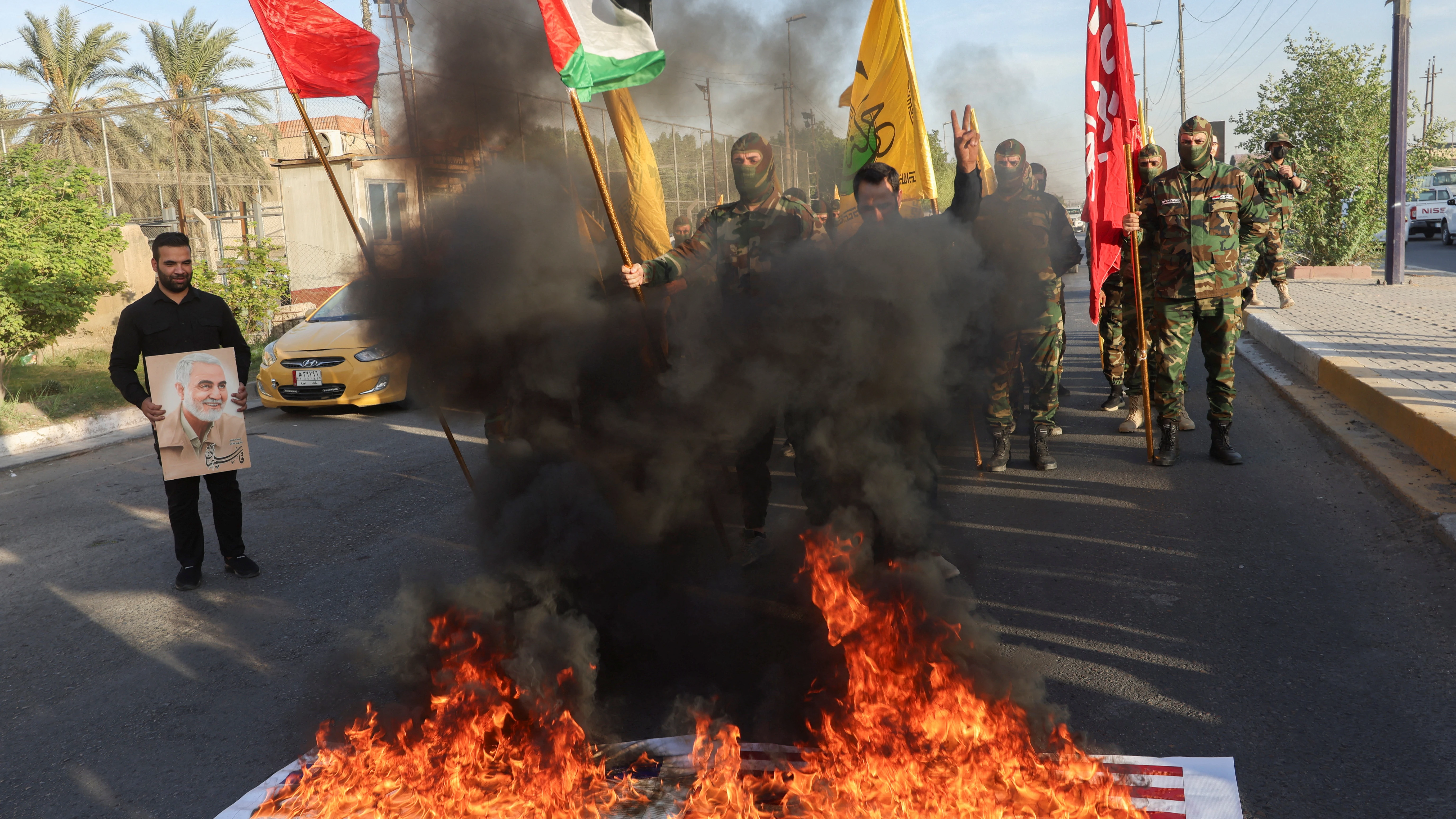 Las banderas nacionales de Estados Unidos e Israel arden, mientras miembros de Harakat Hezbollah al Nujaba se reúnen junto al fuego durante una protesta en solidaridad con los palestinos en Gaza, en Bagdad.