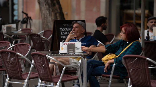 Un hombre fuma sentado en la mesa de una terraza Un hombre fuma sentado en la mesa de una terraza