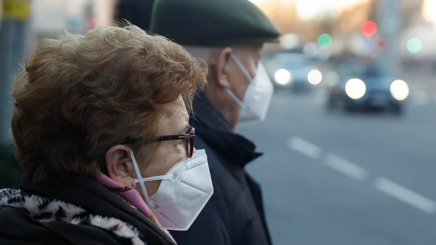 Una pareja de ancianos con mascarillas esperando para cruzar una calle. Una pareja de ancianos con mascarillas esperando para cruzar una calle.