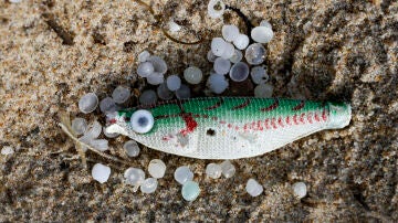 Un pez sintético, empleado como señuelo de pesca, entre varios pellets de plástico en la playa de Ber, del concello coruñés de Pontedeume.