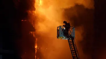 Un bombero trata de apagar el edificio en llamas con dos personas en un balcón, en el barrio de Campanar, a 22 de febrero de 2024, en Valencia