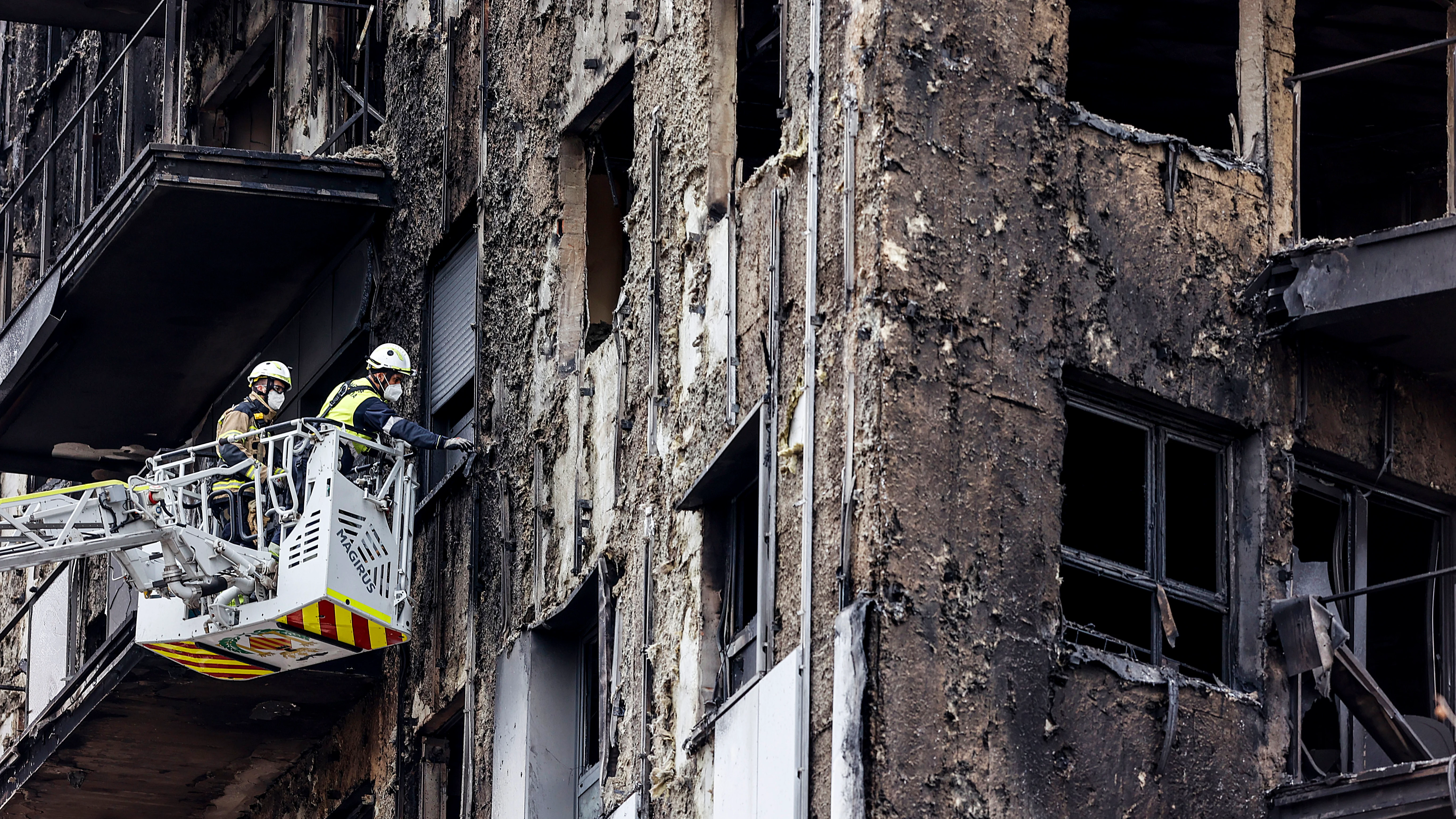 Bomberos en una grúa sanean la fachada del edificio incendiado en Campanar, Valencia