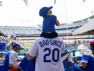 Un padre con una camiseta que pone &#39;Padre desde los 20&#39; con su hijo a hombros en un partido de Los Angeles Dodgers