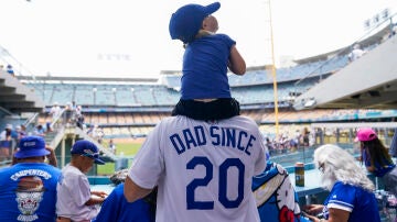 Un padre con una camiseta que pone 'Padre desde los 20' con su hijo a hombros en un partido de Los Angeles Dodgers