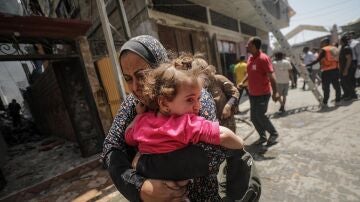 Una mujer palestina que sostiene a un niño en brazos huye del lugar tras un ataque aéreo israelí en el campo de refugiados de Al Nuseirat, en el centro de la Franja de Gaza.
