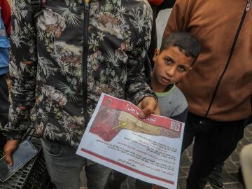 Los palestinos sostienen un folleto lanzado por un avión militar del ejército israelí al este de la ciudad de Rafah, ordenándoles evacuar