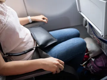 Mujer en un avión con el bolso debajo del asiento Mujer en un avión con el bolso debajo del asiento