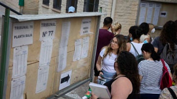 Varias personas miran los carteles con indicaciones para realizar las pruebas para docentes en el IES Butarque de Leganés, Madrid