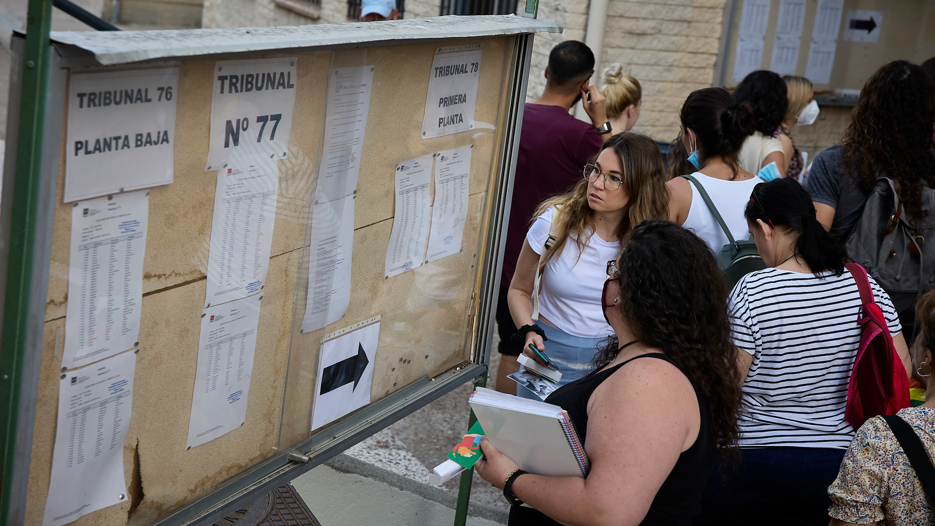 Varias personas miran los carteles con indicaciones para realizar las pruebas para docentes en el IES Butarque de Leganés, Madrid