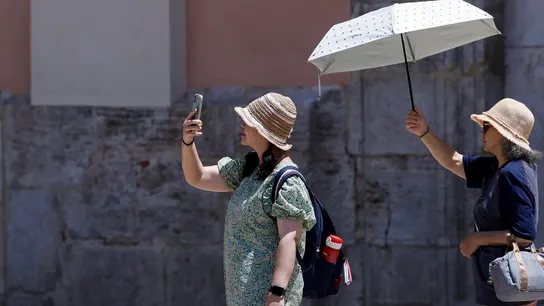 Dos turistas sen protegen del sol y del calor con un parasol durante la mañana de este martes en Valencia. Dos turistas sen protegen del sol y del calor con un parasol durante la mañana de este martes en Valencia.