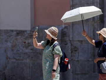 Dos turistas sen protegen del sol y del calor con un parasol durante la mañana de este martes en Valencia. 