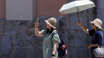 Dos turistas sen protegen del sol y del calor con un parasol durante la mañana de este martes en Valencia. 