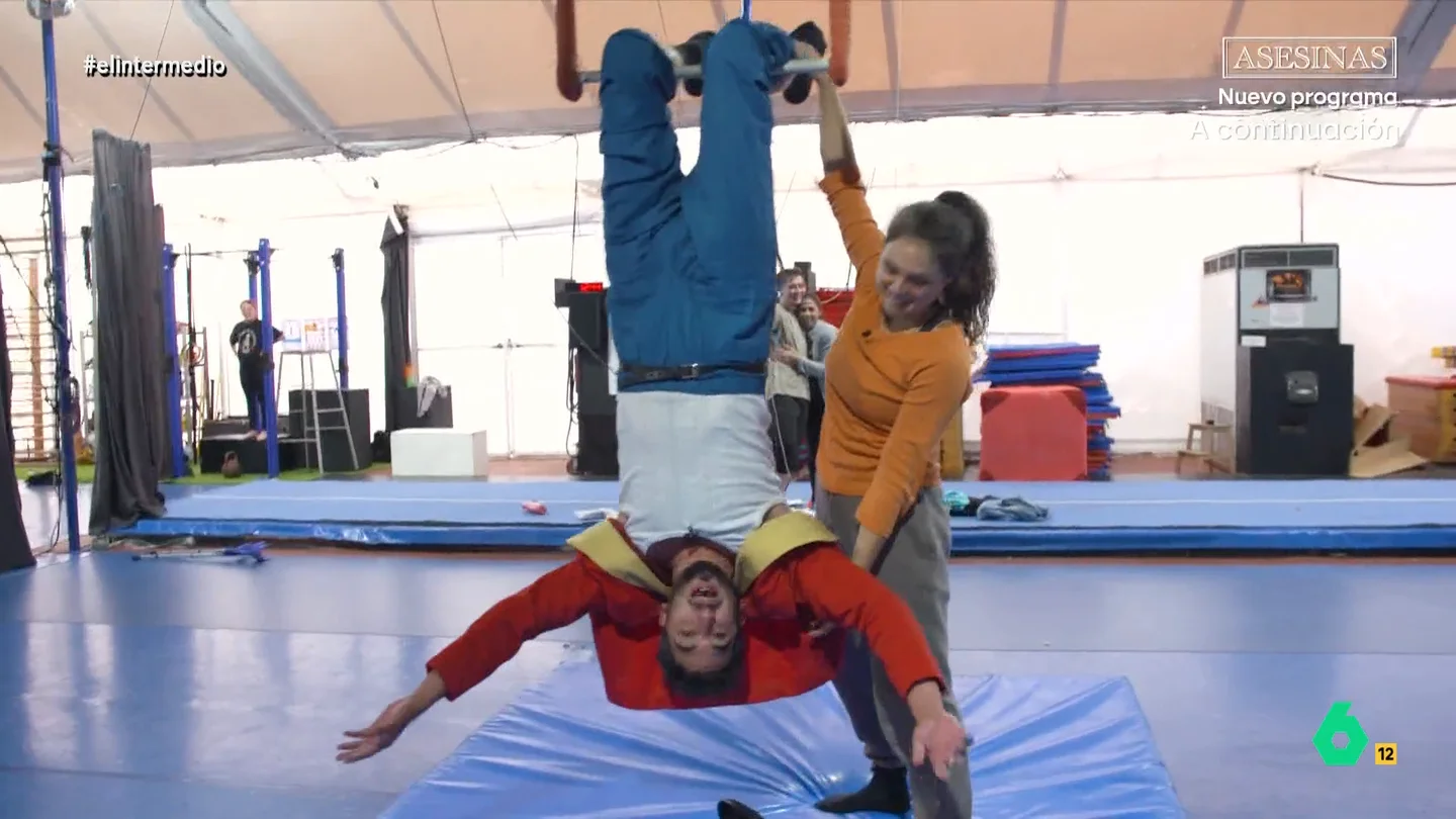 La 'propuesta' de Zenaida, profesora de trapecio, a Isma Juárez: "¿Quieres conocer el dolor?" El reportero se atreve a probar el trapecio, un elemento clásico del circo. A pesar de sus miedos, el reportero consigue colgarse del trapecio e, incluso, suelta las manos.
