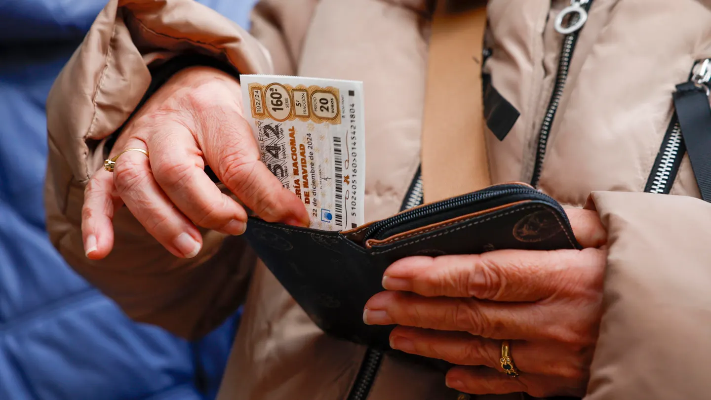Una persona guarda un billere de lotería de Navidad en su cartera. Una persona guarda un billere de lotería de Navidad en su cartera.