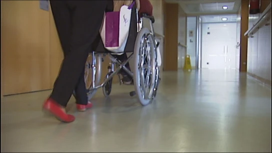 Una trabajadora lleva a una persona en una silla de ruedas Una trabajadora lleva a una persona en una silla de ruedas