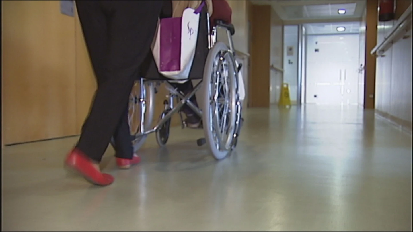 Una trabajadora lleva a una persona en una silla de ruedas Una trabajadora lleva a una persona en una silla de ruedas