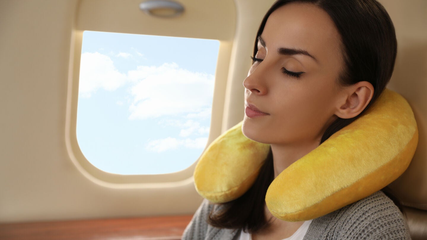 Mujer joven con almohada o coj&iacute;n de viaje en el avi&oacute;n