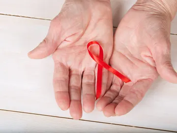 Manos de persona mayor y el lazo contra el VIH Manos de persona mayor y el lazo contra el VIH
