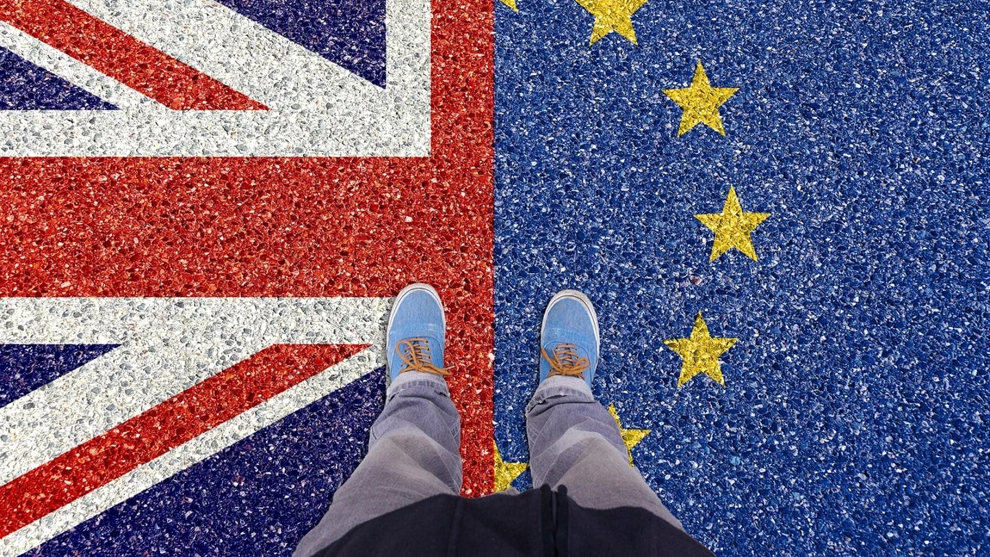Nuevos requisitos para viajar a Reino Unido: qué es la Autorización Electrónica de Viaje y cómo puedo solicitarla. Una persona se detiene sobre el asfalto, donde aparece pintada la mitad de la bandera europea y la mitad de la bandera de Reino Unido.