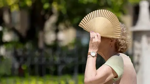 Una mujer se protege del sol con un abanico. Una mujer se protege del sol con un abanico.
