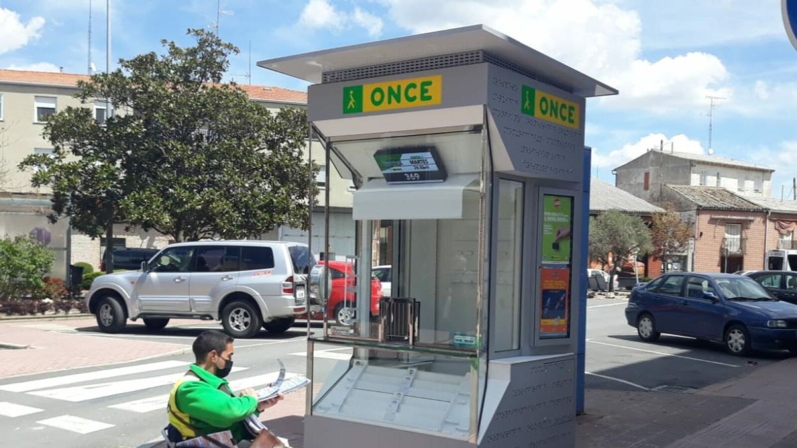 Un vendedor de la ONCE en silla de ruedas comprueba sus cupones junto a un kiosko y punto de venta de la ONCE.
