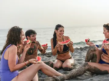 Grupo de amigos comiendo fruta en la playa Grupo de amigos comiendo fruta en la playa