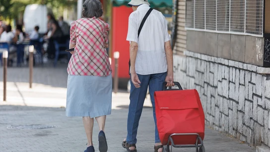 Una pareja camina llevando un carro de la compra. Una pareja camina llevando un carro de la compra.