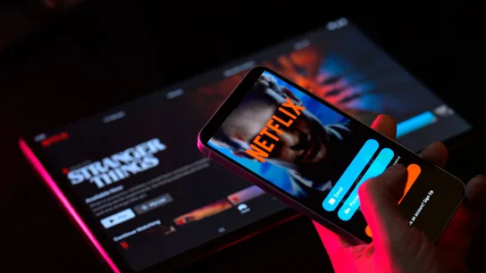 Netflix elimina su Plan Básico sin anuncios en España a partir de septiembre. Un usuario inicia sesión en su cuenta de Netflix en un dispositivo móvil mientras mira Stranger Things en su pantalla del ordenador.
