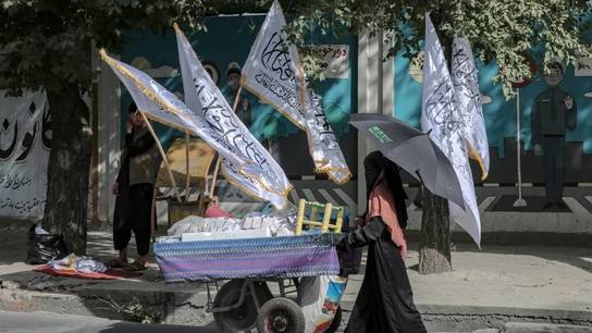 Una mujer empuja un carrito junto a las banderas del Emirato Islámico de Afganistán (Archivo) Una mujer empuja un carrito junto a las banderas del Emirato Islámico de Afganistán