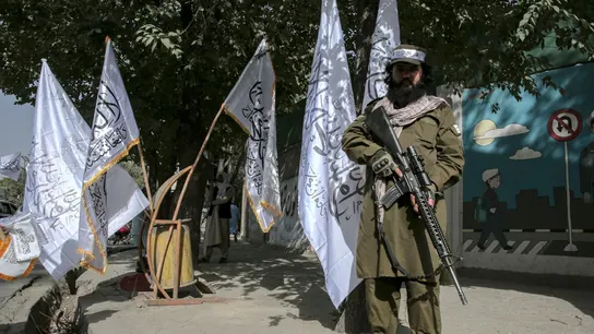 Un miembro de seguridad talibán armado hace guardia junto a las banderas del Emirato Islámico de Afganistán Un miembro de seguridad talibán armado hace guardia junto a las banderas del Emirato Islámico de Afganistán