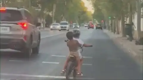 Dos niños circulan sin casco en una bici eléctrica por una concurrida avenida de Sevilla: "Vamos a casa" Dos niños circulan sin casco en una bici eléctrica por una concurrida avenida de Sevilla: "Vamos a casa"