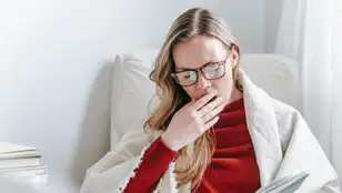 Mujer bostezando bajo una manta mientras lee