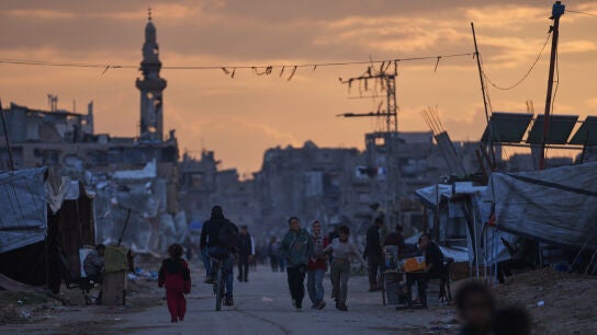 J&oacute;venes palestinos caminan junto a un campamento de desplazados al atardecer en Nuseirat, en el centro de la Franja de Gaza, este viernes.