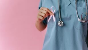 Primer plano de una mano sujetando un lazo rosa, s&iacute;mbolo del c&aacute;ncer de mama.