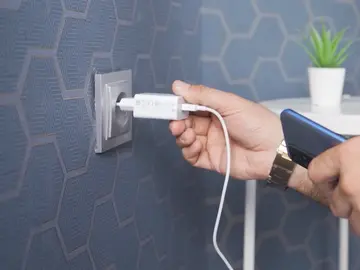 Persona enchufando el cargador a la pared Persona enchufando el cargador a la pared