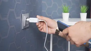 Persona enchufando el cargador a la pared Persona enchufando el cargador a la pared
