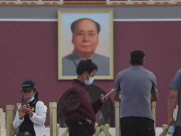 Un joven mira su tel&eacute;fono bajo la mirada de Mao en Tiananmen, en Pek&iacute;n.