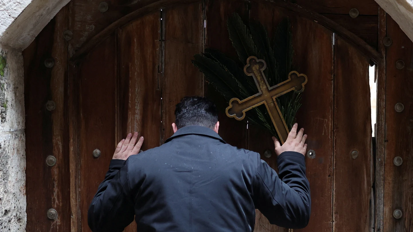 Issa Kassissieh, un cristiano palestino, sostiene una cruz y una rama de palma frente a las puertas de la Iglesia del Santo Sepulcro tras encontrarlas cerradas. Issa Kassissieh, un cristiano palestino, sostiene una cruz y una rama de palma frente a las puertas de la Iglesia del Santo Sepulcro tras encontrarlas cerradas.