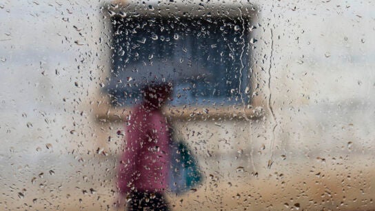 Una persona vista a trav&eacute;s de un cristal mojado camina bajo la lluvia en una imagen de archivo. 