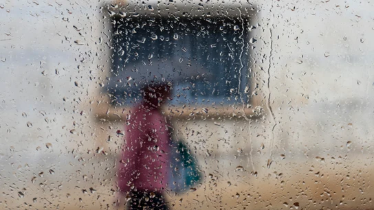 Una persona vista a través de un cristal mojado camina bajo la lluvia en una imagen de archivo. Una persona vista a través de un cristal mojado camina bajo la lluvia en una imagen de archivo.