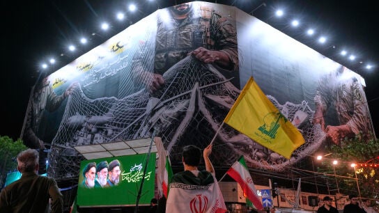 Un manifestante iran&iacute; ondea una bandera de Hizbul&aacute; bajo una valla que muestra aviones estadounidenses cayendo en la red de pesca de las fuerzas armadas iran&iacute;es