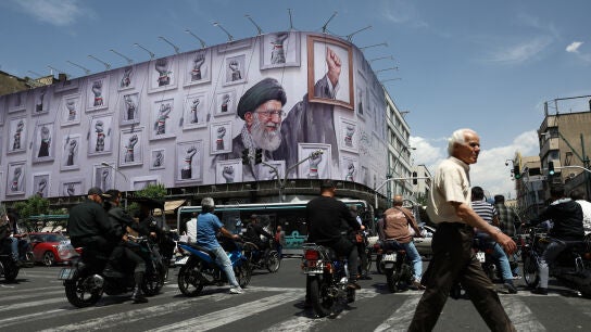 Varias personas circulan cerca de una valla con una imagen del difunto l&iacute;der supremo de Ir&aacute;n, el ayatol&aacute; Ali Khamenei, en Teher&aacute;n