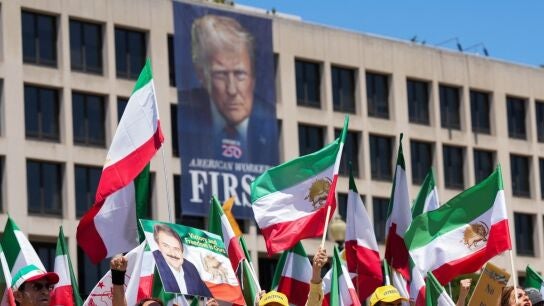 Personas con banderas de Ir&aacute;n con una pancarta de Trump detr&aacute;s