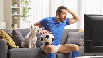 Un hombre viendo el f&uacute;tbol con su perro al lado